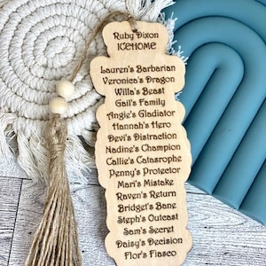 May include: A wooden bookmark with a tassel, featuring the name "Ruby Dixon Icehome" and a list of names with descriptive words, such as "Lauren's Barbarian", "Veronica's Dragon", and "Willa's Beast".