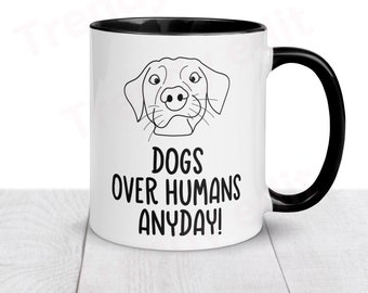 May include: White ceramic coffee mug with a black rim and handle. The mug features a black and white line drawing of a dog's head and the text "Dogs over humans anyday!"
