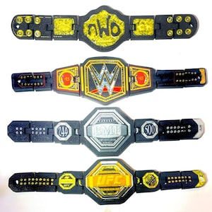 May include: Four toy championship belts are shown. The belts are black with gold and silver detailing. The top belt has "nWo" in yellow. The second belt has "WWE" in silver and red. The third belt has "BMI" and numbers. The bottom belt has "UFC" in yellow.