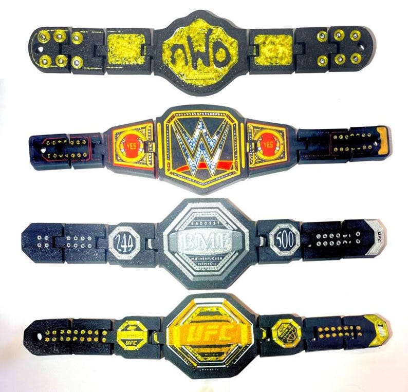 May include: Four toy championship belts are shown. The belts are black with gold and silver detailing. The top belt has "nWo" in yellow. The second belt has "WWE" in silver and red. The third belt has "BMI" and numbers. The bottom belt has "UFC" in yellow.