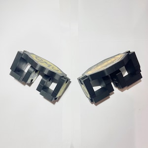 May include: Two black, geometric objects with a gold design. The objects appear to be made of plastic or a similar material. The design on each object is circular and has a yellow and gold colour scheme.