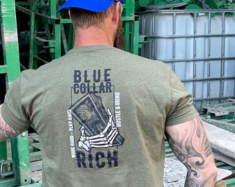 Puede incluir: Una camiseta verde con un gráfico de una mano esquelética sosteniendo una pila de dinero. El texto en la camiseta dice "Blue Collar Rich" y "Work Hard - Play Hard - Hustle & Grind".