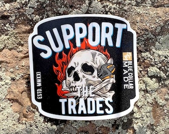 May include: A black and white sticker with a skull wearing a wrench and a bandana. The skull is on fire and the text "SUPPORT THE TRADES" is written in white letters. The text "ESTD. MMXXI" is written in white letters on the left side of the sticker. The text "BLUE COLLAR MADE" is written in white letters on the right side of the sticker.