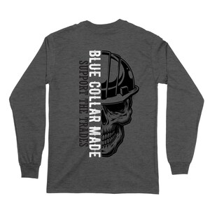 May include: Dark gray long-sleeve shirt featuring a detailed skull wearing a hard hat. The text "BLUE COLLAR MADE SUPPORT THE TRADES" is printed vertically on the left side of the skull graphic. The shirt is made of a soft, comfortable material.