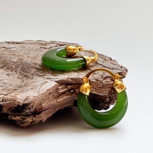 May include: A pair of green hoop earrings with gold accents. The earrings are made of a smooth, rounded material and have a simple, elegant design.