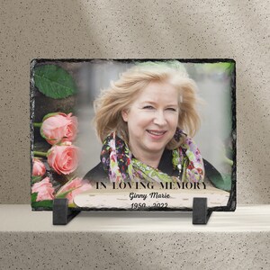 May include: A slate memorial plaque with a photo of a woman and pink roses. The plaque reads "In Loving Memory Ginny Marie 1950 - 2022".