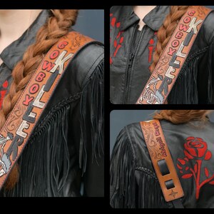 May include: A brown leather guitar strap with the words "Cowboy Killer" embroidered in red and black. The strap has a fringe design and is decorated with a skull and crossbones.