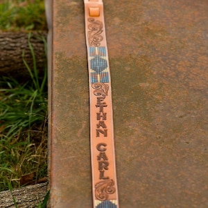 May include: A brown leather guitar strap with a blue and white beaded design. The strap is personalised with the name "ETHAN CARL" in a decorative font.