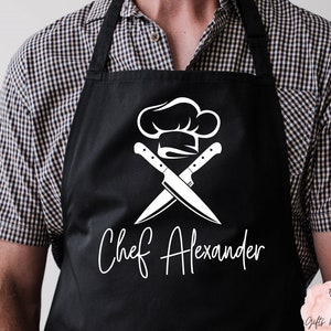 May include: Black apron with a white chef hat and crossed knives design. The text "Chef Alexander" is printed below the design.