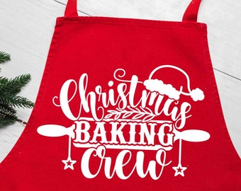 May include: A red apron with the words "Christmas Baking Crew" in white script. The design includes a Santa hat, rolling pin, and stars. A sprig of evergreen is in the upper left corner.