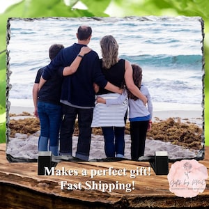 May include: A family of four standing on a beach, looking out at the ocean. The family is wearing casual clothing and is holding each other close. The image is printed on a slate tile with a rustic, natural look.