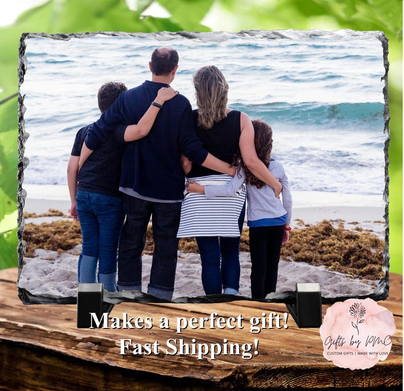 May include: A family of four standing on a beach, looking out at the ocean. The family is wearing casual clothing and is holding each other close. The image is printed on a slate tile with a rustic, natural look.