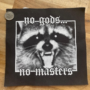 May include: Black square patch with a white raccoon graphic and the text "no-gods... no-masters". The raccoon is in a square frame. A U.S. dime is next to the patch for size comparison.