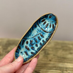 Puede incluir: Plato de cerámica hecho a mano con forma de hoja, con un esmalte turquesa brillante y detalles marrones. El plato tiene una superficie texturizada y una estética natural y terrosa. Perfecto para guardar objetos pequeños.