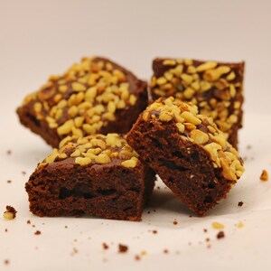 Peut inclure: Quatre brownies au chocolat garnis de noix hach&eacute;es sur une surface blanche.