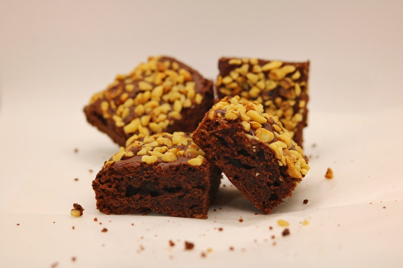 Peut inclure: Quatre brownies au chocolat garnis de noix hach&eacute;es sur une surface blanche.