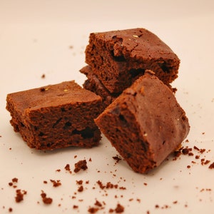 Peut inclure: Quatre brownies au chocolat sur une surface blanche. Les brownies sont d'une couleur brun fonc&eacute; et ont une texture l&eacute;g&egrave;rement friable. Il y a aussi quelques miettes de brownie sur la surface.