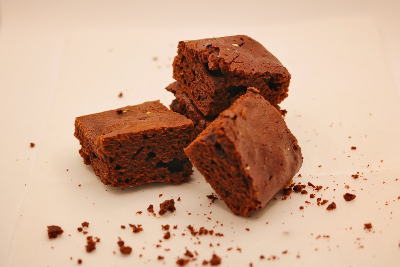 Peut inclure: Quatre brownies au chocolat sur une surface blanche. Les brownies sont d'une couleur brun fonc&eacute; et ont une texture l&eacute;g&egrave;rement friable. Il y a aussi quelques miettes de brownie sur la surface.
