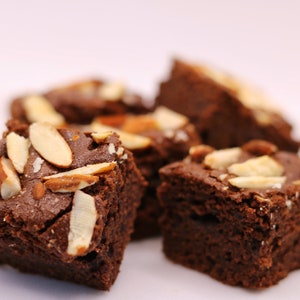 Peut inclure: Gros plan sur quatre brownies au chocolat garnis d'amandes effil&eacute;es. Les brownies sont dispos&eacute;s sur une surface blanche.