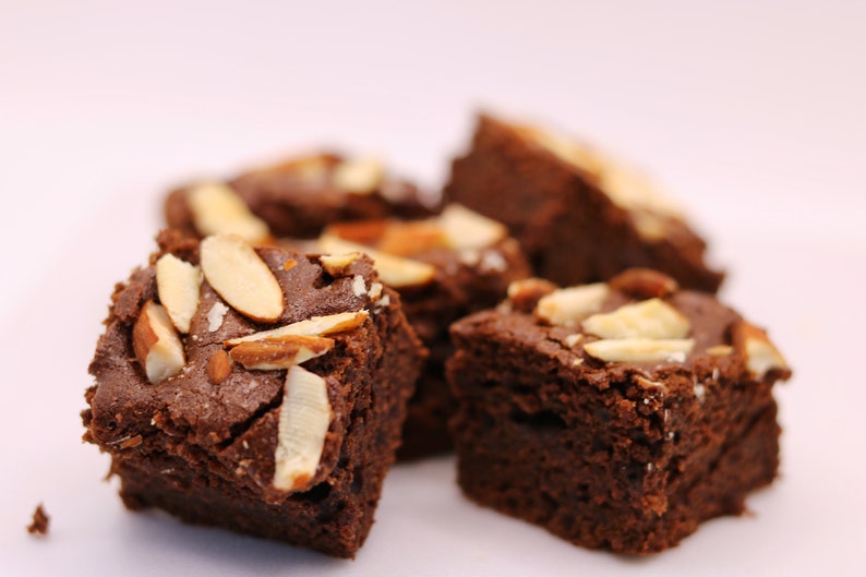 Peut inclure: Gros plan sur quatre brownies au chocolat garnis d'amandes effil&eacute;es. Les brownies sont dispos&eacute;s sur une surface blanche.
