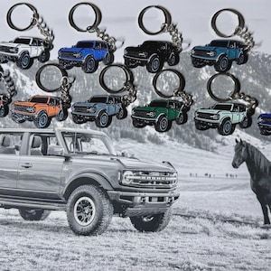 Peut inclure: Une collection de porte-clés SUV colorés avec des anneaux argentés. Les porte-clés sont de différentes couleurs, dont blanc, bleu, noir, rouge, orange, vert et sarcelle. Un grand SUV gris et un cheval noir en arrière-plan.