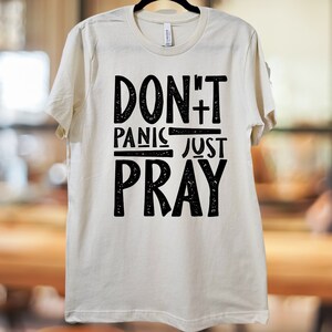 May include: A white t-shirt with black text that reads "Don't Panic Just Pray".