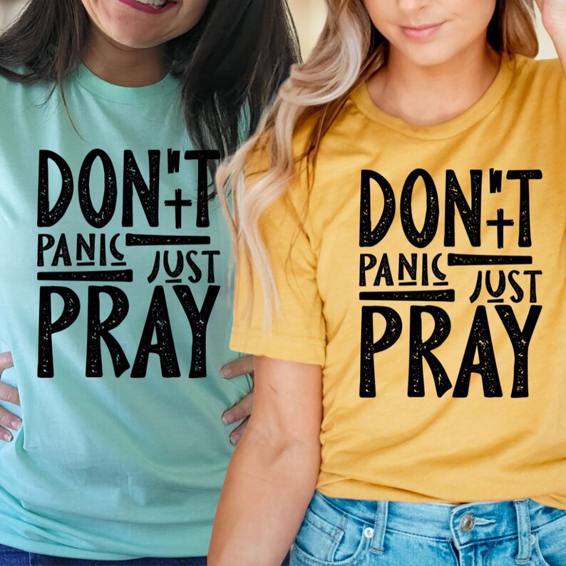 May include: Two women wearing t-shirts with the text "Don't Panic Just Pray" in black distressed lettering on a light blue and yellow background.