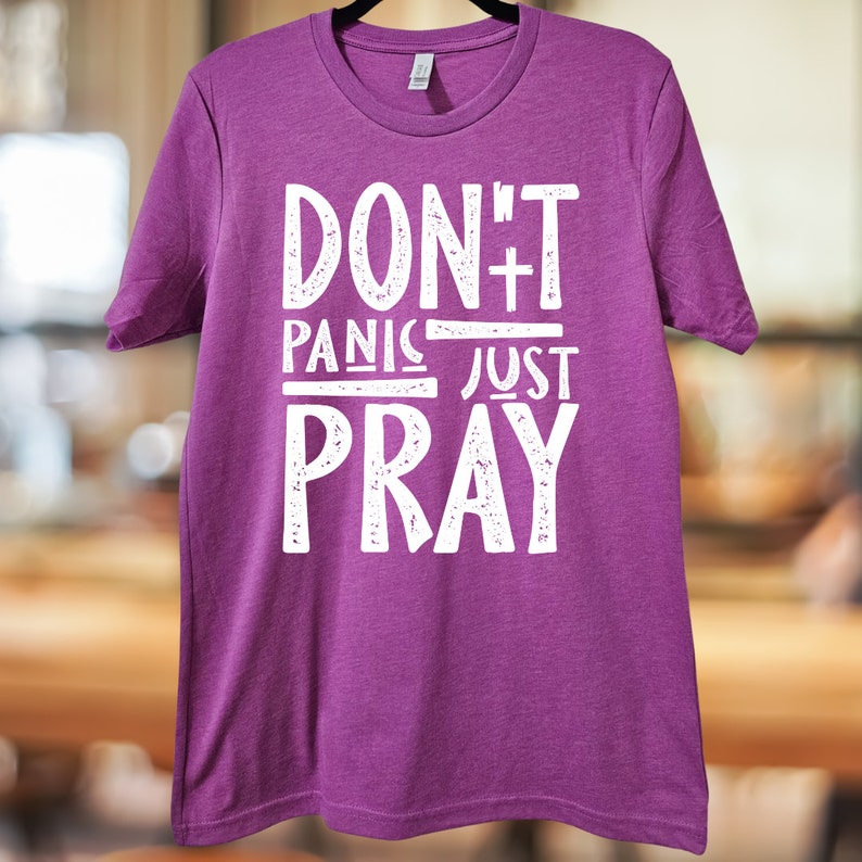May include: Purple t-shirt with white text that reads "Don't Panic Just Pray".