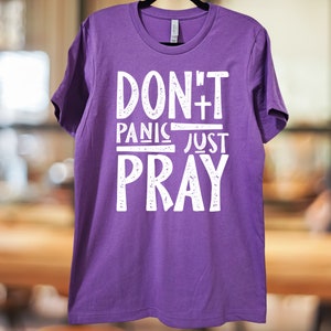 May include: Purple t-shirt with white text that reads "Don't Panic Just Pray" with a cross symbol.
