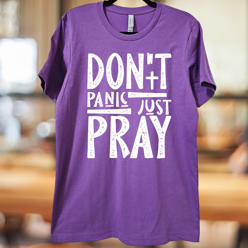May include: Purple t-shirt with white text that reads "Don't Panic Just Pray" with a cross symbol.