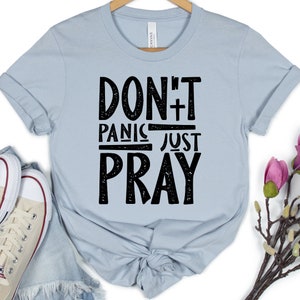 May include: A light blue t-shirt with a black graphic that says "Don't Panic Just Pray" with a cross symbol.