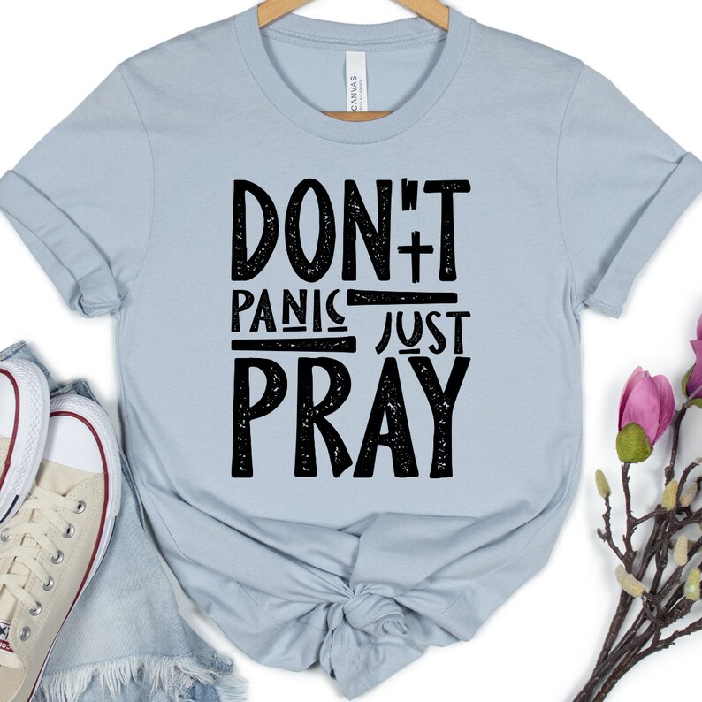 May include: A light blue t-shirt with a black graphic that says "Don't Panic Just Pray" with a cross symbol.