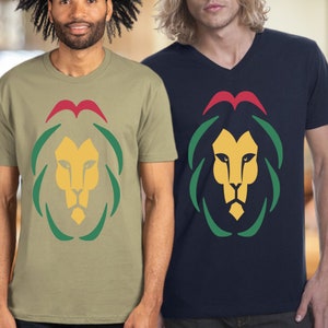 May include: Two t-shirts with a lion graphic. The lion is yellow with a red mane and green leaves. One shirt is khaki and the other is navy blue.