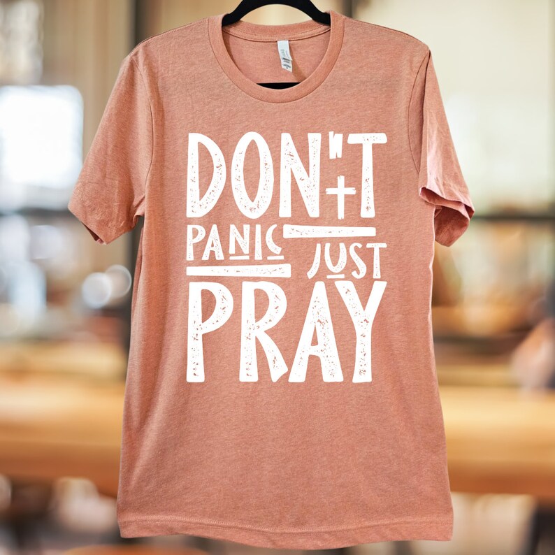May include: A peach-coloured t-shirt with the text "Don't Panic Just Pray" in white distressed lettering.