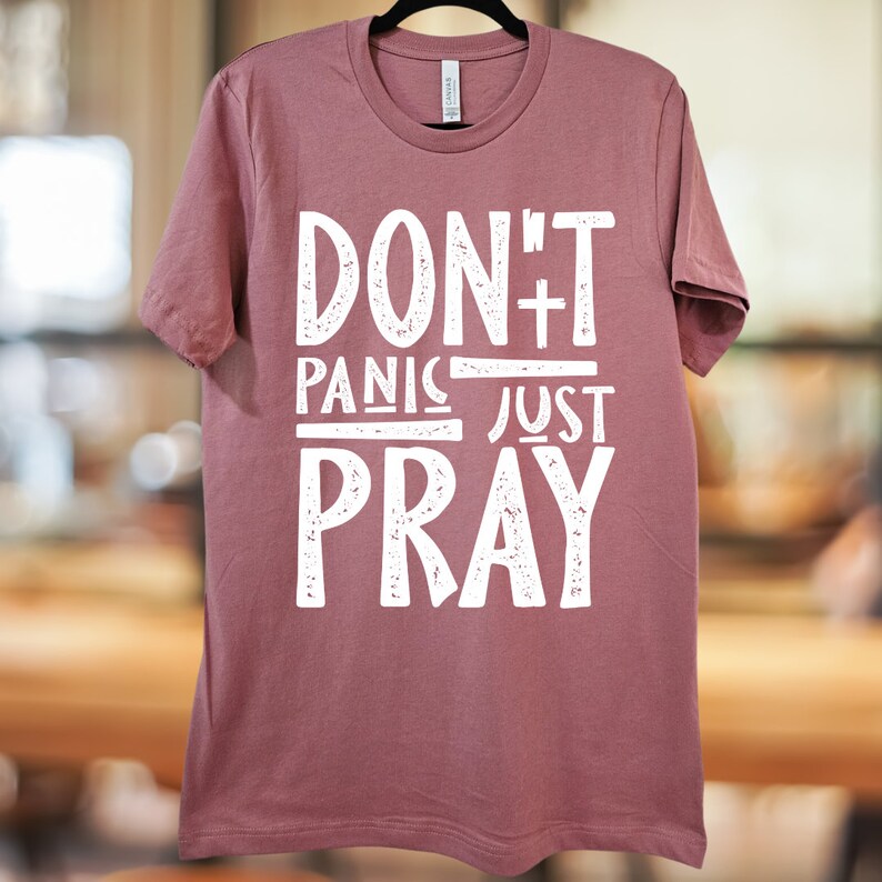 May include: A mauve t-shirt with the text "Don't Panic Just Pray" in white distressed lettering.