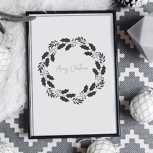 May include: A black framed print with a white background and a black silhouette of a holly wreath with the text "Merry Christmas" in gold lettering.