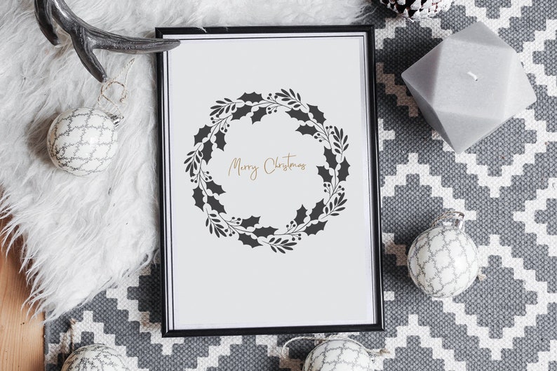May include: A black framed print with a white background and a black silhouette of a holly wreath with the text "Merry Christmas" in gold lettering.