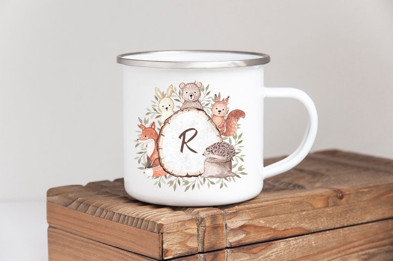 May include: White enamel mug with a woodland animal design. The design features a fox, bear, rabbit, squirrel, and hedgehog around a tree stump with the letter "R" on it.