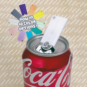 May include: A white plastic TabBuddy tool attached to the metal pull tab of a red Coca-Cola soda can. A circular display shows ten different colored versions of the same tool with the text "now in 10 color options!" printed in the center.