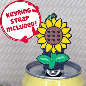 May include: A sunflower keyring with yellow petals, a brown centre with heart details, and green leaves. The keyring is attached to a green loop. Text in a red circle reads "KEYRING STRAP INCLUDED!"