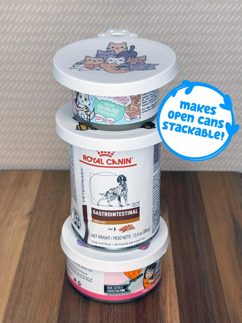May include: A stack of three pet food cans with white plastic lids featuring a cartoon cat illustration. The middle can is Royal Canin Veterinary Gastrointestinal Low Fat dog food. A blue circular graphic with the text makes open cans stackable!
