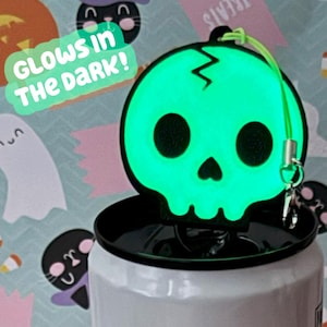 May include: A glowing green skull-shaped accessory with a lightning bolt design, attached to a black lid. The text "GLOWS IN THE DARK!" is visible. The accessory is on a white container, with a Halloween-themed background.