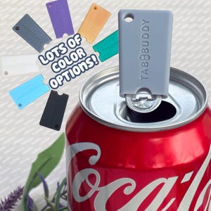 May include: A light gray TabBuddy can opener tool attached to the metal tab of a red soda can. The image includes the text LOTS OF COLOR OPTIONS! and displays several additional TabBuddy tools in white, blue, black, purple, orange, and green.