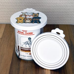 May include: A white plastic pet food can lid featuring a colorful cartoon illustration of various dog breeds on top, positioned next to a Royal Canin Veterinary Gastrointestinal Low Fat dog food can with a matching white lid attached.