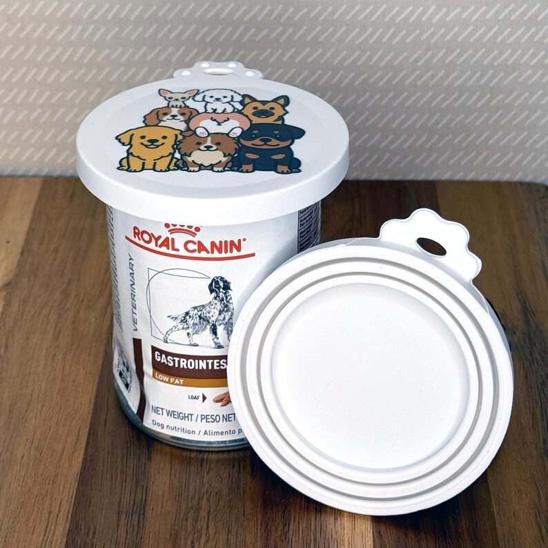 May include: A white plastic pet food can lid featuring a colorful cartoon illustration of various dog breeds on top, positioned next to a Royal Canin Veterinary Gastrointestinal Low Fat dog food can with a matching white lid attached.