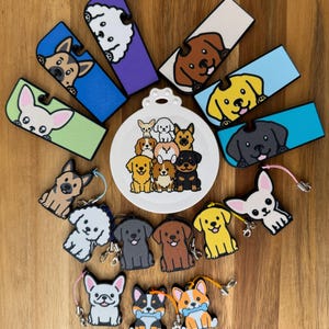 May include: A collection of rectangular and dog-shaped silicone keychains and accessories featuring various dog breeds in colors including blue, purple, green, yellow, and white, centered around a white circular plate with a group of illustrated dogs.
