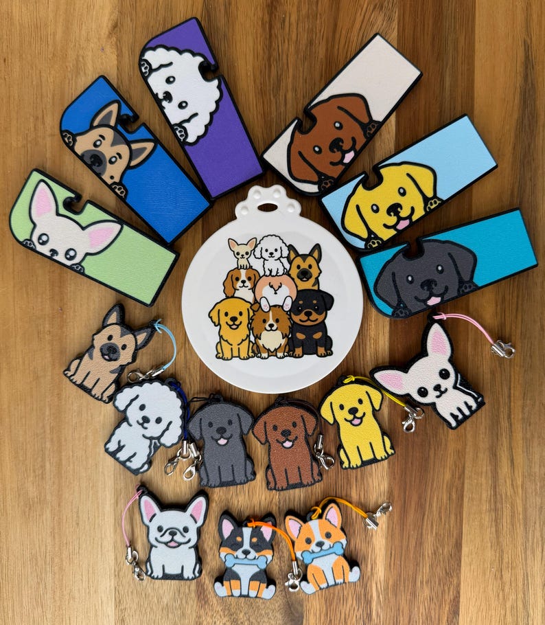 May include: A collection of rectangular and dog-shaped silicone keychains and accessories featuring various dog breeds in colors including blue, purple, green, yellow, and white, centered around a white circular plate with a group of illustrated dogs.