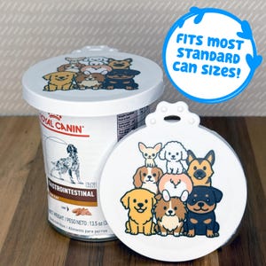 May include: A white circular plastic pet food can lid featuring a colorful cartoon illustration of seven different dog breeds. The lid has a small tab at the top and is designed to fit most standard can sizes, as indicated by the blue circular text.