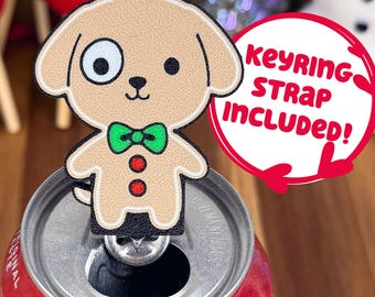 May include: A tan dog-shaped keychain with a green bow tie and red buttons, attached to a silver keyring. The keychain is placed on top of a red soda can. The text "KEYRING STRAP INCLUDED!" is in a red circle.