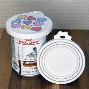 May include: A Royal Canin Veterinary Gastrointestinal Low Fat dog food can with a white plastic lid featuring colorful heart illustrations. A second identical white plastic lid with a tabbed edge is positioned to the right of the food can.